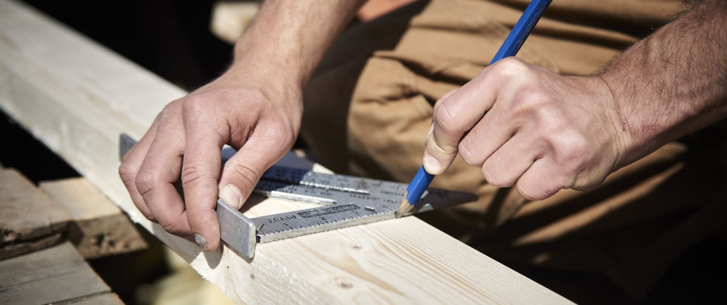 Håndværker opmåler trækonstruktion med vinkelmåler og blyant