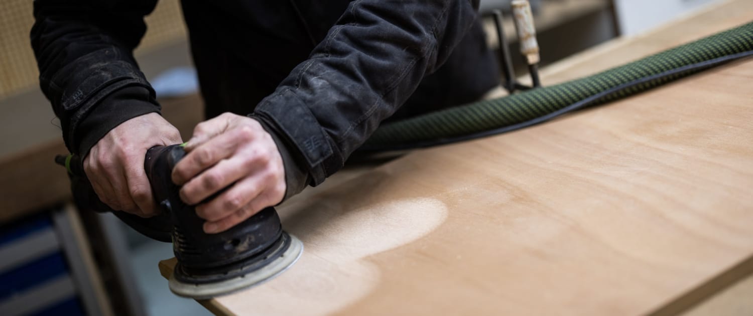 Snedker i arbejdstøj sliber overflade på træbord