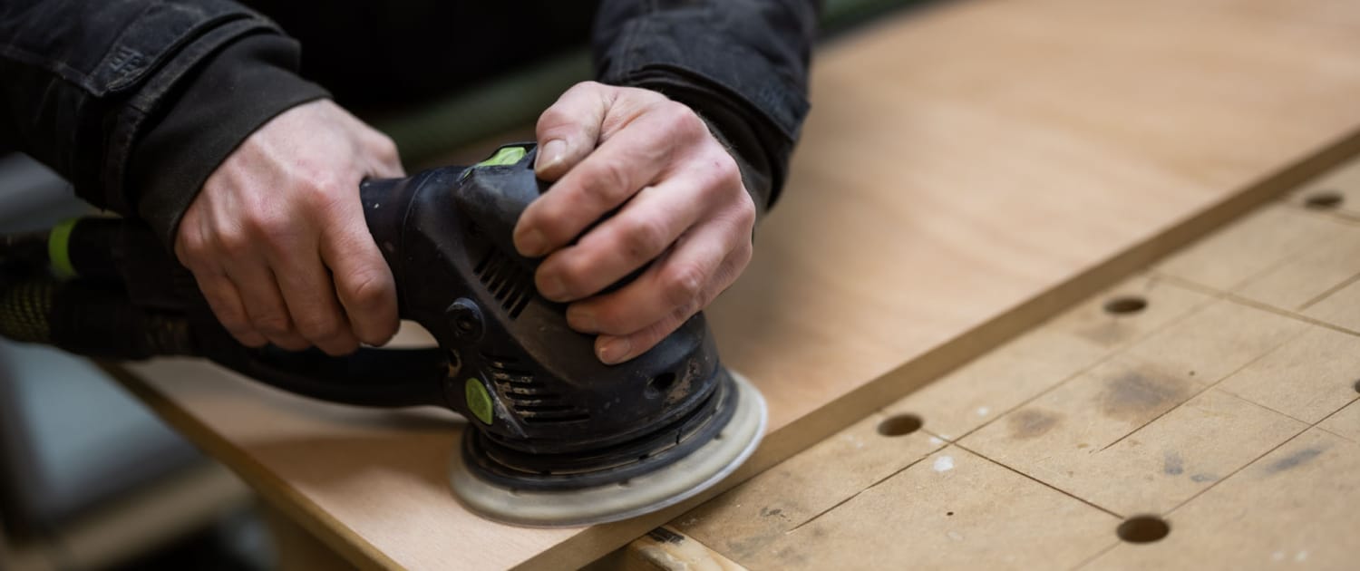 Snedker i arbejdstøj sliber overflade på træbord