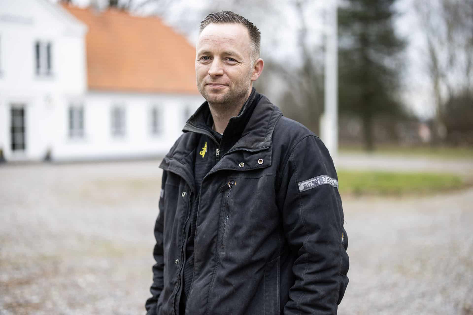 Snedkermesteren foran hvid hovedbygning på godset